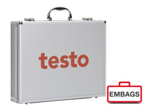 Eine silberne Hartschalen-Aktentasche mit schwarzem Griff, auf deren Vorderseite das Wort testo in großen orangefarbenen Buchstaben steht. Ideal für den B2B-Einsatz, mit einem rot-weißen EMBAGS-Logo und einem Koffersymbol in der rechten unteren Ecke.