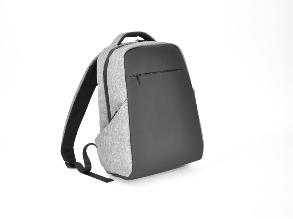 A modern backpack with a grey outer material and black front, with a zippered pocket on the front and a single adjustable shoulder strap on a white background - ideal for B2B professionals looking for an alternative to the classic aluminum case.