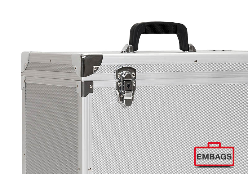 Eine Nahaufnahme eines silbernen Alu-Boxenkoffers mit verstärkten Ecken, einem schwarzen Griff und einem Schnappverschluss. Das EMBAGS-Logo mit der roten Kofferkontur befindet sich unten rechts - perfekt für B2B-Bedürfnisse und Sonderanfertigungen.