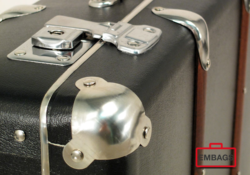 Nahaufnahme eines schwarzen Vintage-Aluminiumkoffers mit glänzenden Metallecken und Verriegelung, mit einem rot-schwarzen "EMBAGS"-Logo in der rechten unteren Ecke - ideal für B2B-Sonderanfertigungen.