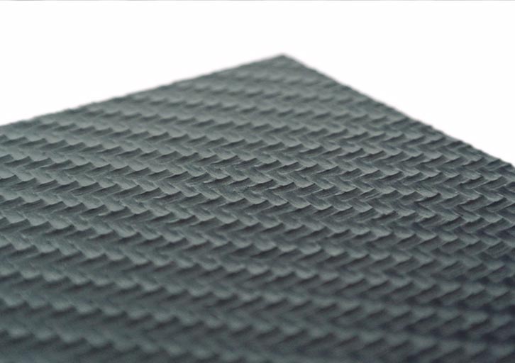 Primer plano de una superficie gris oscura, texturizada, con un dibujo repetido de pequeñas formas cuadradas en relieve dispuestas en cuadrícula. La superficie se muestra en un ángulo que acentúa el efecto tridimensional del dibujo.