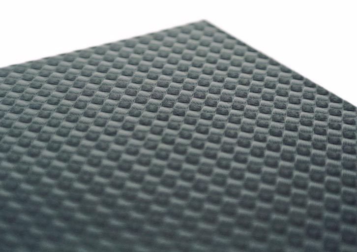 Primer plano de una superficie texturizada de color gris oscuro con un motivo geométrico repetido de pequeños cuadrados en relieve dispuestos en forma de cuadrícula. El dibujo crea una sensación de profundidad y un efecto táctil tridimensional en la superficie.