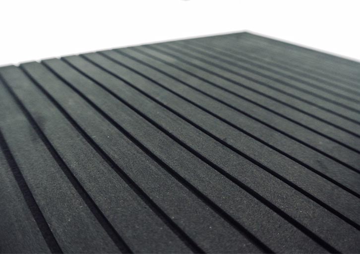 Primer plano oblicuo de una superficie negra con surcos paralelos uniformemente espaciados que van en diagonal desde abajo a la izquierda hasta arriba a la derecha. La iluminación resalta la textura y la profundidad de los surcos y confiere a la superficie un aspecto liso y moderno.