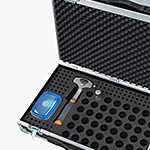A black foam-lined carrying case is open, showing a blue container, a bottle opener with a black handle and orange accent, and a small cylindrical metal object placed in designated slots.